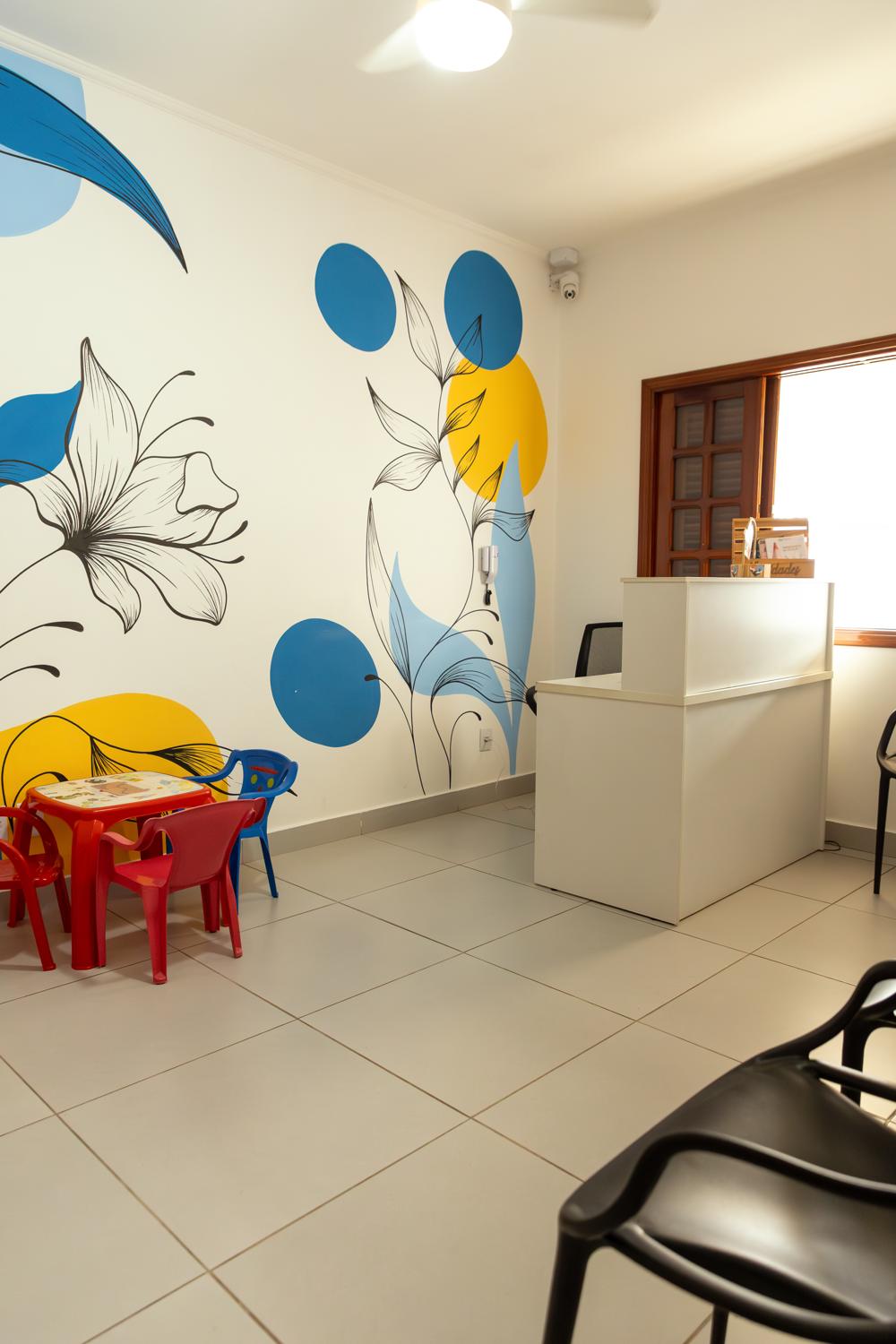 Recepção da Clínica Zelo, com parede pintada de flores e círculos azuis e amarelos